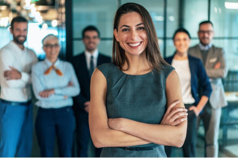Smiling team leader with arms crossed, standing in front of her team in an office
